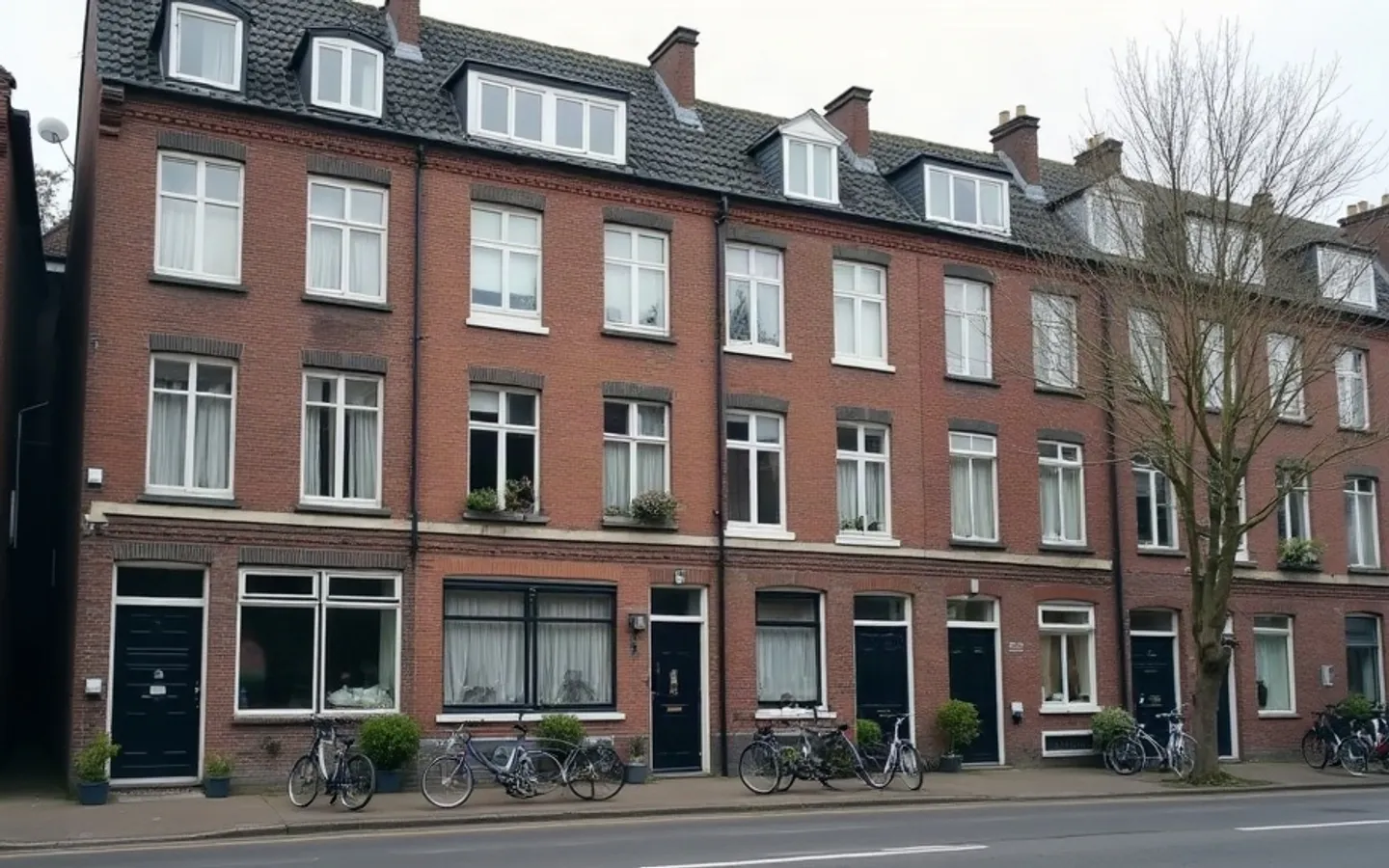 Rij bakstenen appartementengebouwen met verhuurde woningen langs een stille straat, gordijnen dicht in enkele ramen en fietsen bij de entrees.